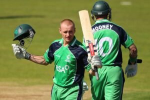 Ireland cricket player William Porterfield in Irish cricket jersey in with his bat raising in one hand and the helmet in another hand.